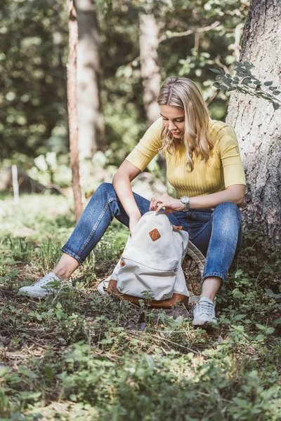 Young woman looking for something in backpack in forest — Stock Photo