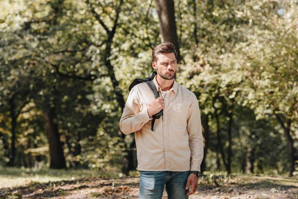 Portrait of pensive young man with backpack standing in autumn park — Stock Photo