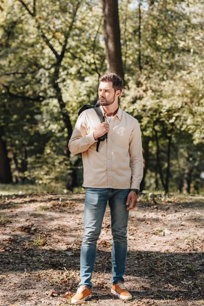 Stilvoller junger Mann mit Rucksack steht im Herbstpark — Stockfoto