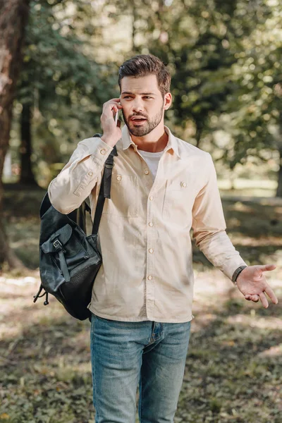 Portrait of man with backpack talking on smartphone in park — Stock Photo