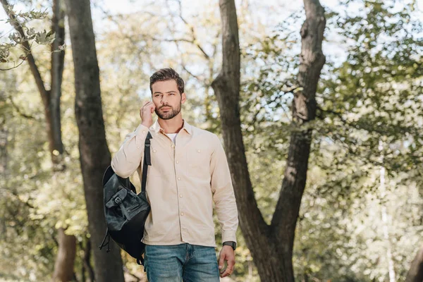 Portrait of young man with backpack talking on smartphone in park — Stock Photo