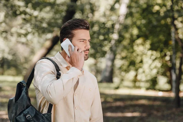 Visão lateral do jovem com mochila falando no smartphone no parque — Fotografia de Stock