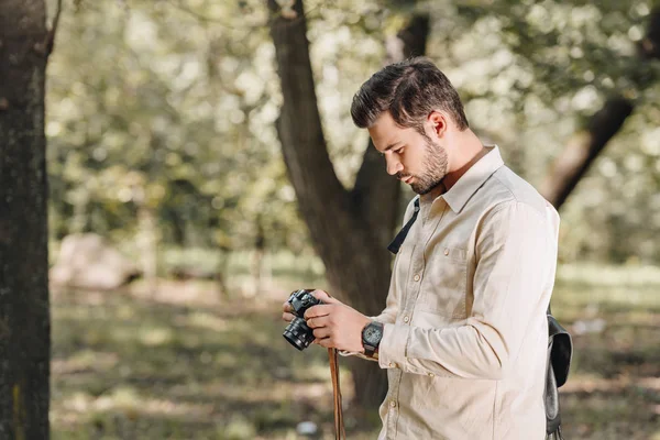 Side view of tourist with photo camera in hands in autumn park — Stock Photo