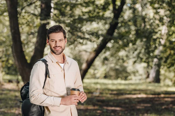 Porträt eines lächelnden Mannes mit Rucksack und Coffee to go im Park — Stockfoto