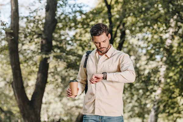 Портрет людини з рюкзаком і кавою, щоб піти перевірити час в парку — стокове фото