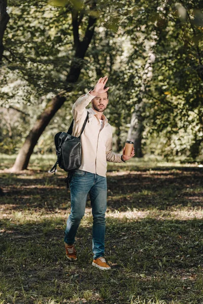 Homme élégant avec sac à dos et café pour aller saluer quelqu'un dans le parc — Photo de stock
