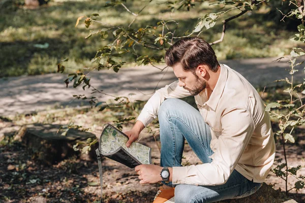 Side view of young traveler looking for destination on map in park — Stock Photo