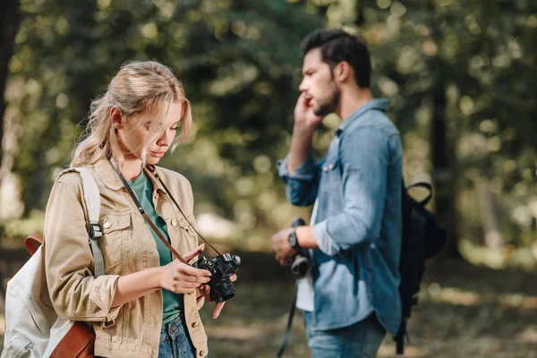 Selective focus of woman with photo camera and man talking on smartphone in park — Stock Photo