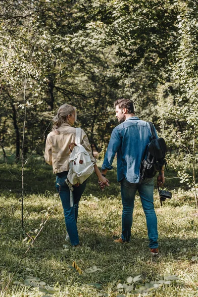Rückansicht eines romantischen Paares mit Rucksäcken, die sich Händchen haltend im Park — Stockfoto