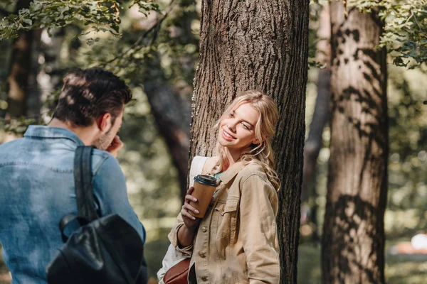 Чоловік фотографує усміхнену дівчину з кавою, щоб піти в парк — стокове фото