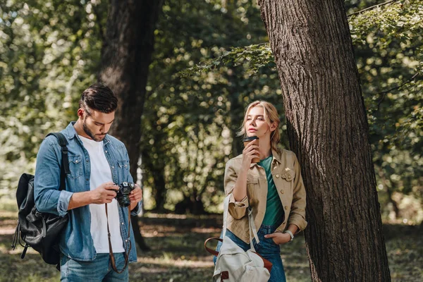 Portrait of pensive woman with coffee to go and man with photo camera in park — Stock Photo