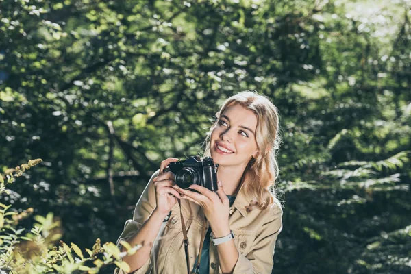 Портрет улыбающейся женщины с фотокамерой в парке — стоковое фото