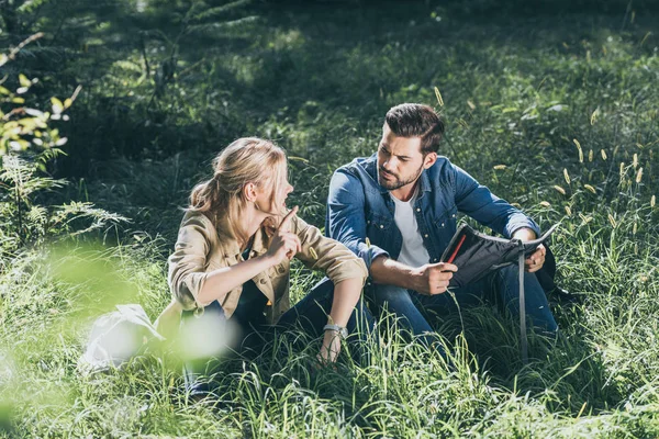 Couple de jeunes voyageurs avec carte se reposant sur l'herbe dans le parc — Photo de stock