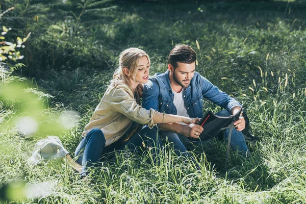 Paar junger Reisender mit Karte ruht sich im Park auf Gras aus — Stockfoto