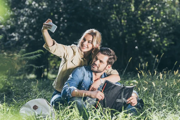 Touristes souriants avec carte prendre selfie sur smartphone dans le parc — Photo de stock