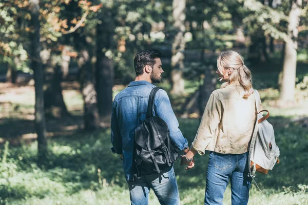 Vista trasera de pareja joven con mochilas caminando en el parque de otoño - foto de stock