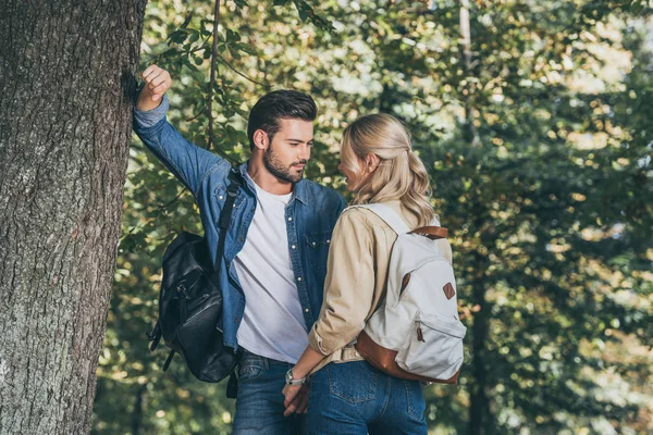 Pareja joven con mochilas mirándose en el parque - foto de stock