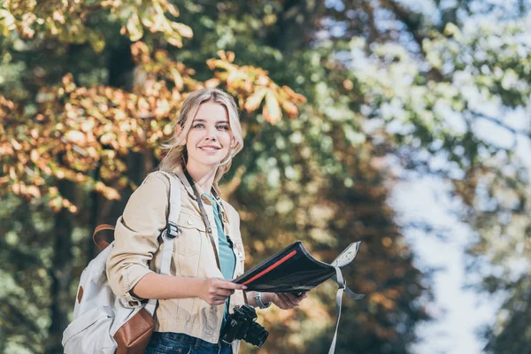 Retrato de jovem viajante sorridente com mochila, câmera de foto e mapa no parque — Fotografia de Stock