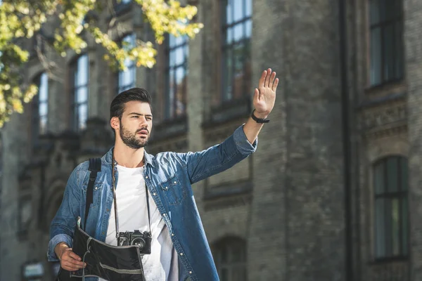 Portrait de jeune touriste avec carte et appareil photo appelant taxi dans la rue — Photo de stock