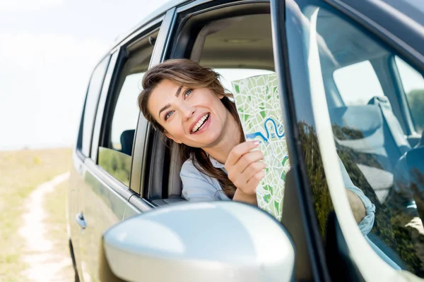 Beautiful happy woman holding travel map inside car in field — Stock Photo