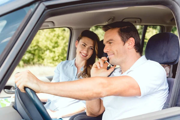 Feliz pareja adulta viajando en coche mientras el hombre habla por teléfono - foto de stock