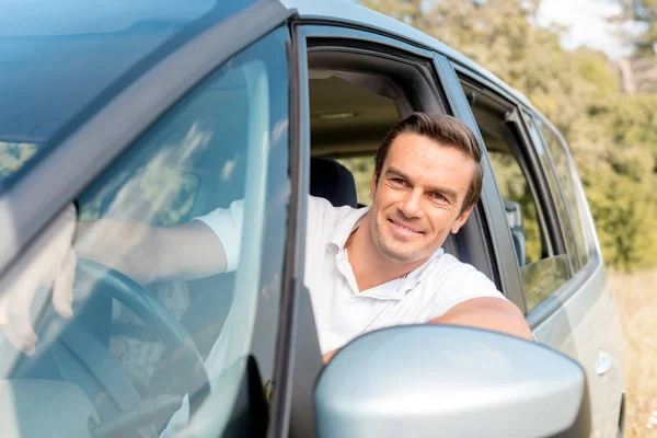 Happy man looking out window while driving car in field — Stock Photo