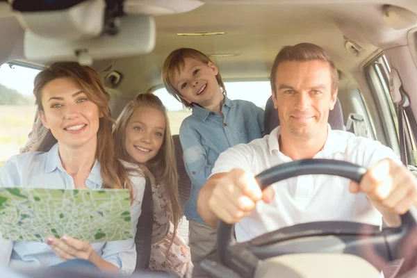 Happy young family looking at camera while travelling by car — Stock Photo