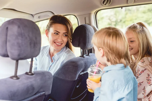 Щаслива мати дивиться на своїх чарівних дітей на задніх сидіннях автомобіля під час поїздки — стокове фото