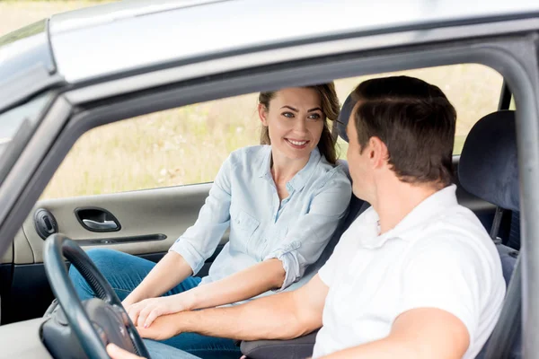 Heureux couple adulte tenant la main tout en étant assis dans la voiture — Photo de stock