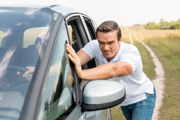 Handsome man pushing his broken car in field — Stock Photo