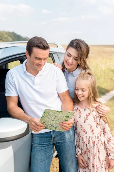 Hermosa familia mirando el mapa juntos durante el viaje en coche en el campo - foto de stock