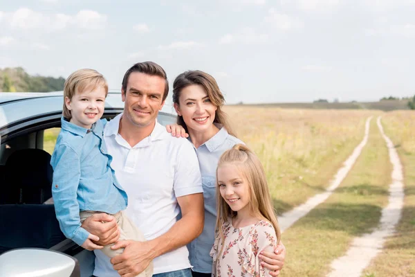 Happy young family with car looking at camera in field — Stock Photo