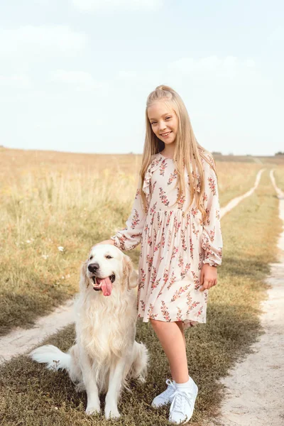 Happy little child with adorable golden retriever dog looking at camera in field — Stock Photo