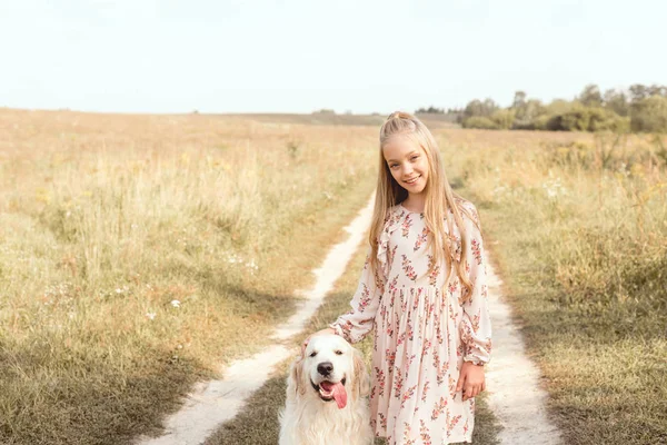 Прекрасный маленький ребенок с очаровательной золотистой собакой-ретривером, смотрящей на камеру в поле — стоковое фото