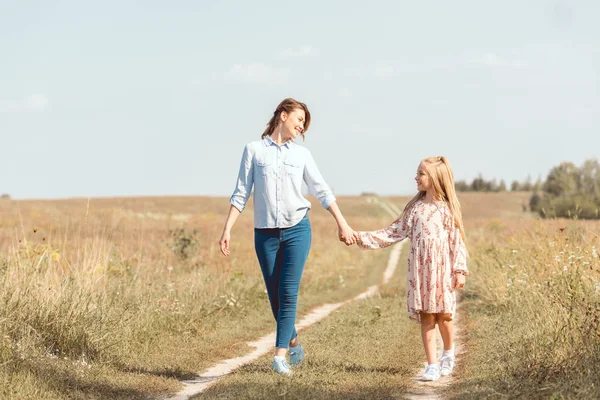 Mère heureuse et fille tenant la main et marchant ensemble dans le champ — Photo de stock