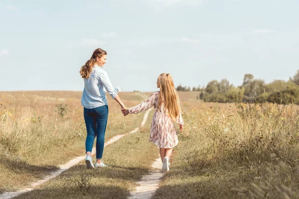 Задний вид матери и дочери, держащихся за руки и идущих вместе в поле — стоковое фото