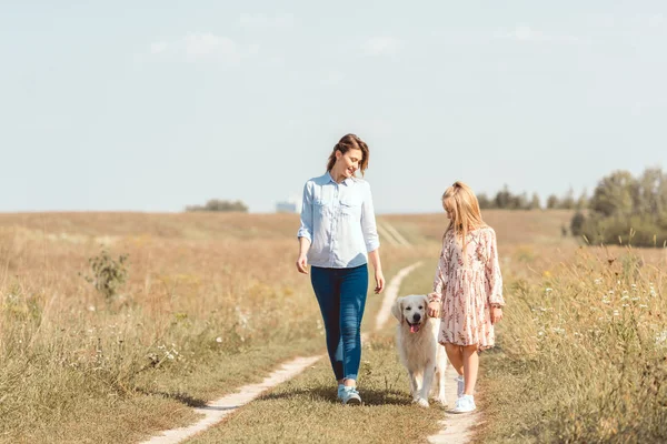 Happy mother and daughter walking with golden retriever in field — Stock Photo