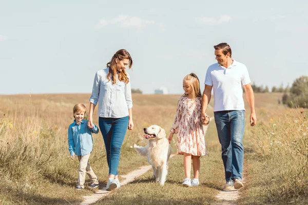 Heureux jeune famille avec chien récupérateur passer du temps ensemble dans le champ — Photo de stock