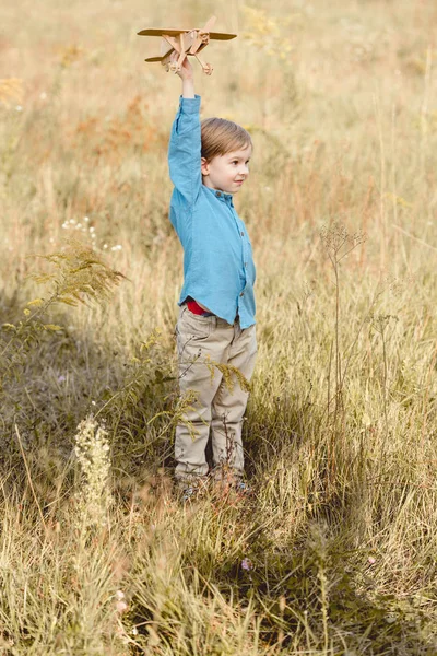 Милый маленький ребенок в поле играет с игрушечным самолетом в поле — стоковое фото