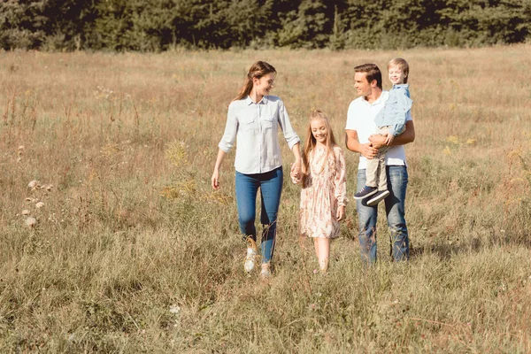 Familia joven y feliz caminando por el campo juntos - foto de stock