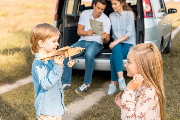 Heureux petits enfants jouer avec jouet avion tandis que les parents naviguant avec la carte et assis dans le coffre de la voiture dans le champ — Photo de stock