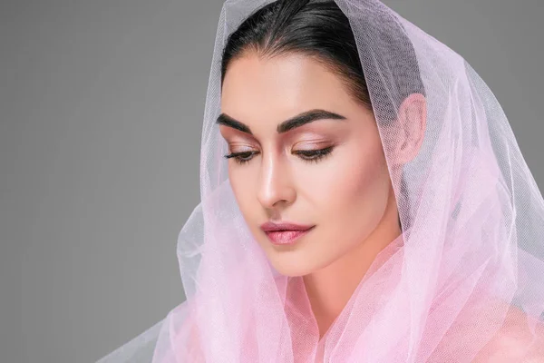 Hermosa joven con velo rosa mirando hacia abajo aislado en gris — Stock Photo