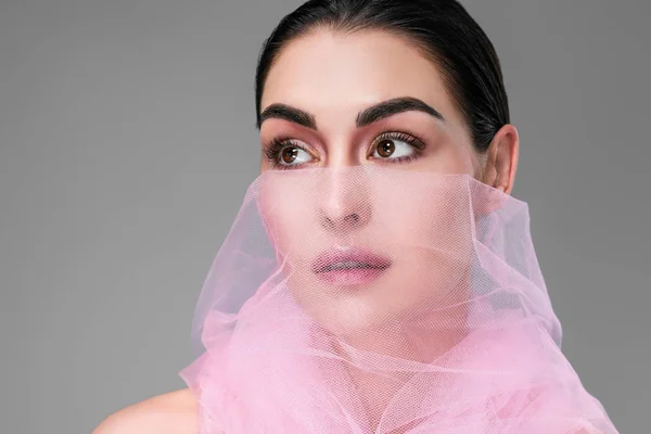 Belle jeune femme avec voile rose sur le visage regardant loin isolé sur gris — Photo de stock