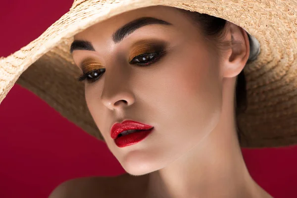 Menina bonita com maquiagem elegante usando chapéu de palha e olhando para baixo isolado no vermelho — Fotografia de Stock