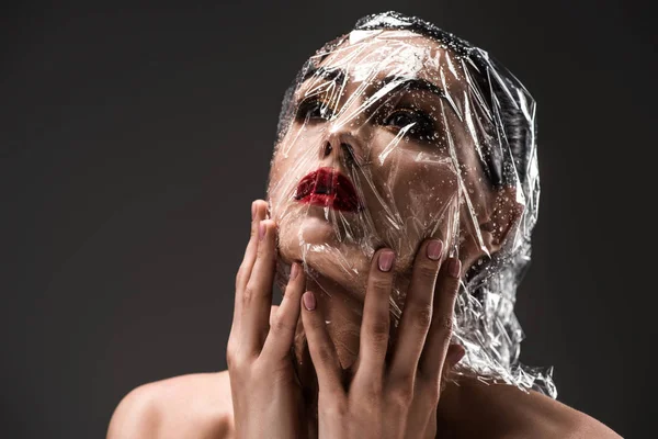 Young woman with face wrapped in wet transparent cellophane isolated on black — Stock Photo