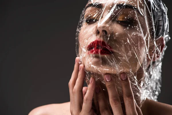 Jeune femme sensuelle avec le visage enveloppé de cellophane transparent humide isolé sur noir — Photo de stock