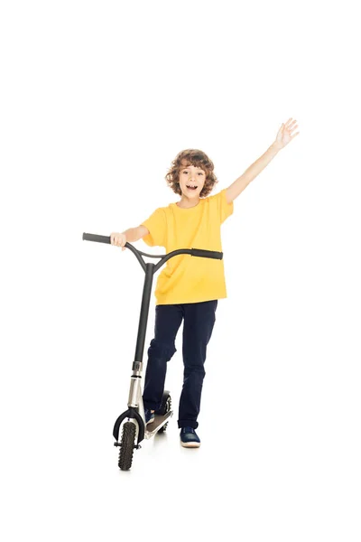 Niño feliz de pie con scooter y levantamiento de la mano aislado en blanco - foto de stock