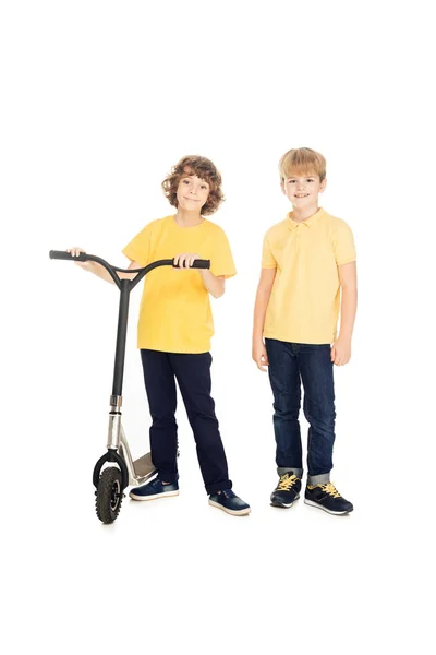 Милые счастливые мальчики стоят со скутером и улыбаются в камеру изолированы на белом — стоковое фото