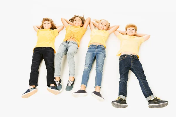 High angle view of adorable happy kids in yellow t-shirts lying together and smiling at camera isolated on white — Stock Photo