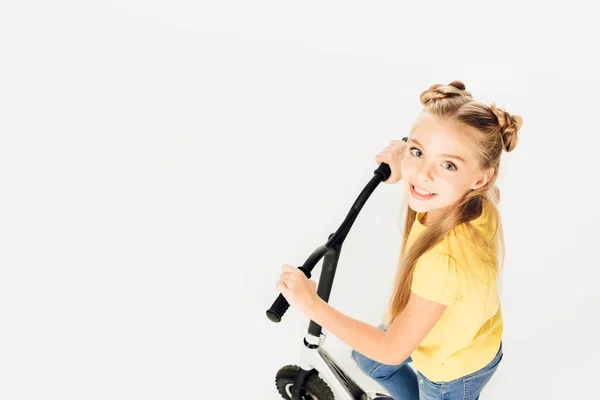 Vista de ángulo alto de adorable niño feliz montando scooter y sonriendo a la cámara aislada en blanco - foto de stock